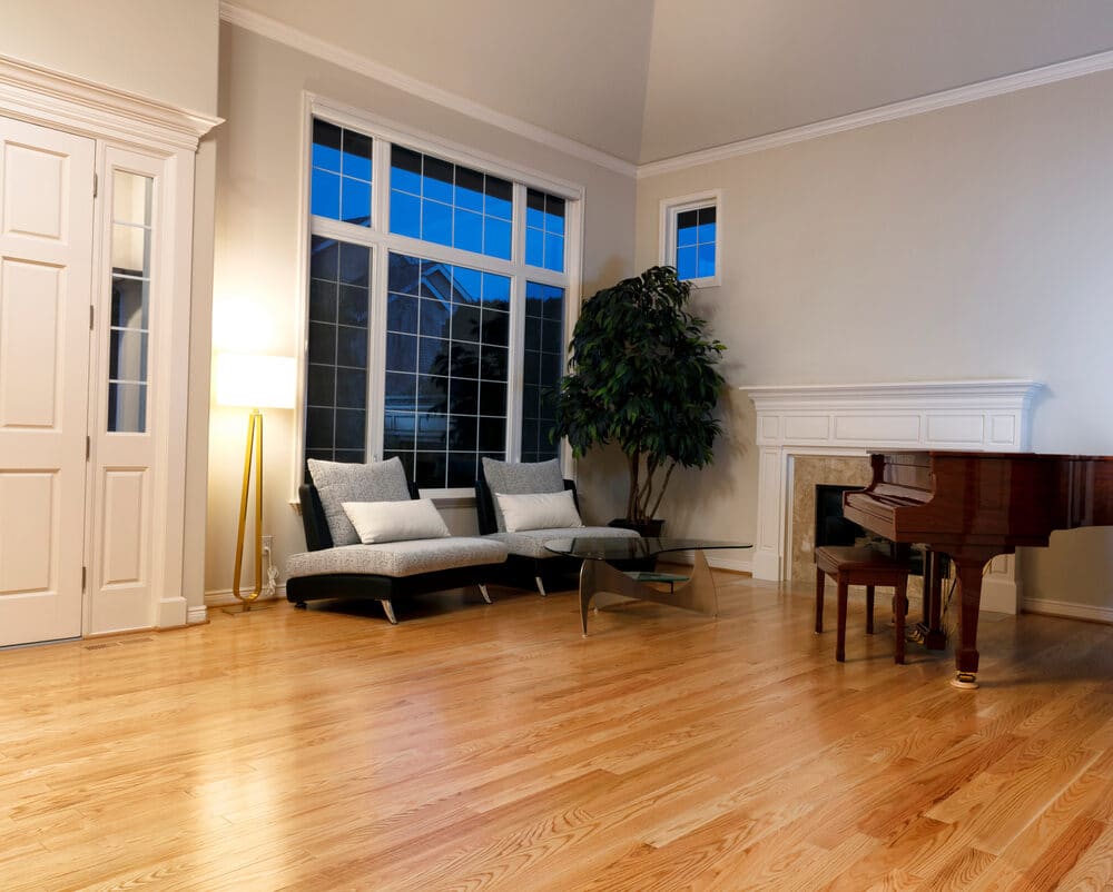 An elegant living room at dusk with a grand piano, large windows, and a sitting area.
