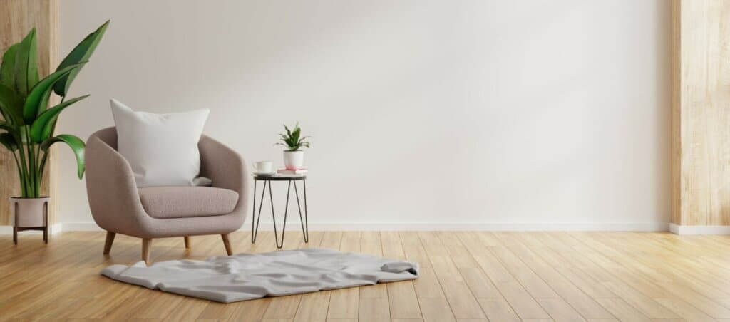 A cozy living room corner featuring a modern beige armchair with a white cushion, a small side table with a potted plant and a cup, and a large green potted plant beside the chair. The room has light wood flooring, expertly sanded and refinished, creating a warm and inviting atmosphere.