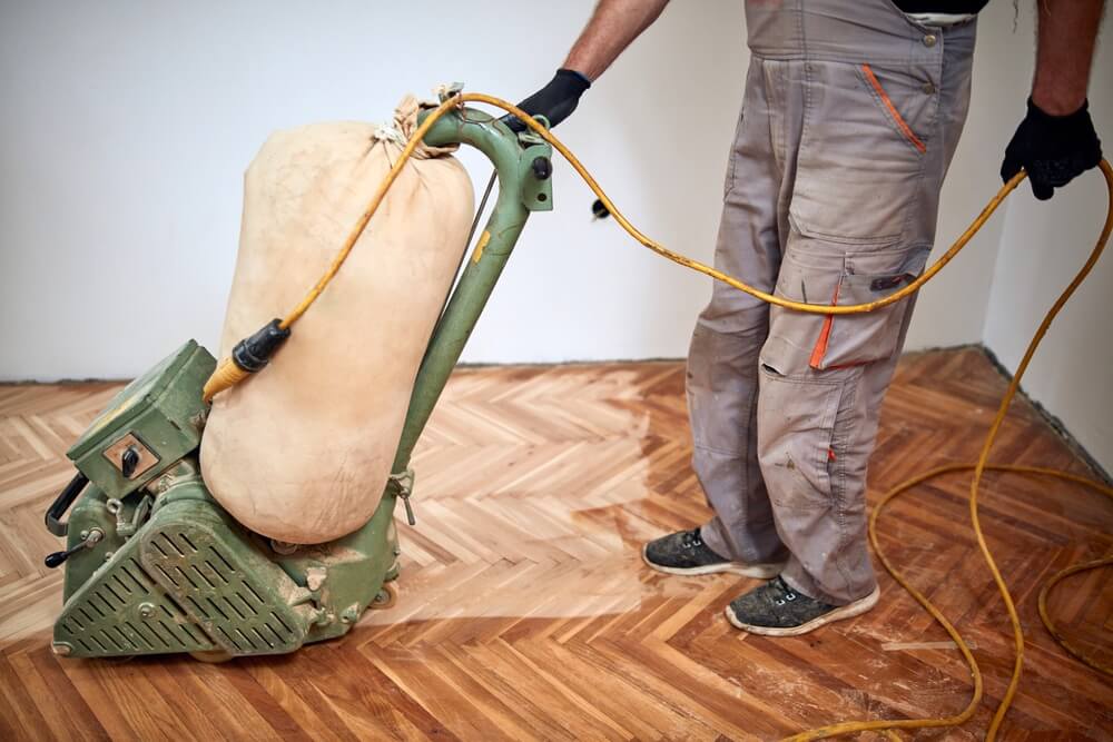 A Mr Sander® technician sanding a parquet floor in a Finchley Church End living room using a LAGLER HUMMEL® machine. Features include powerful LED lighting, high powered aggressive sanding, extremely low dust emissions, quick belt changes, 30+ years lifespan, and easy maintenance. Technical specs: 230 V / 50 CPS / 2.2 kW motor, 200 mm drum width, 2400 rpm drum speed, 200 x 750 mm belt dimensions, 79 kg weight.