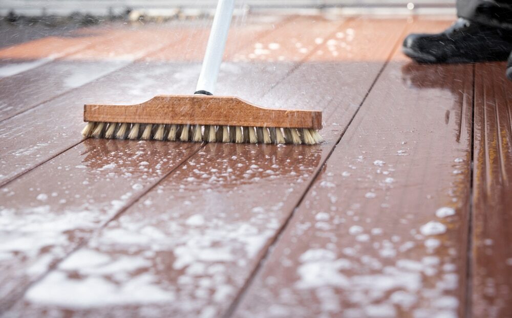 Scrubbing a wet wooden deck with a brush, soap bubbles visible.