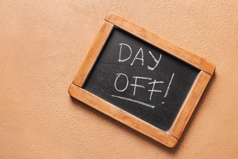 A small chalkboard with a wooden frame displays the words "DAY OFF!" written in white chalk. The chalkboard is placed against a textured, tan-colored wall, positioned at an angle.