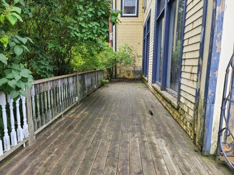 A wooden deck with a railing overlooks a lush green backyard with a swimming pool and patio.