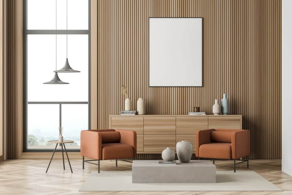 A modern living room with a minimalist design featuring two orange armchairs, a wooden sideboard, and decorative vases. The room has a large window allowing natural light to fill the space, and the walls are adorned with vertical wooden slats. The beautifully finished light wood herringbone floor complements the clean and stylish aesthetic, showcasing the quality of Mr Sander®'s floor sanding and refinishing services.