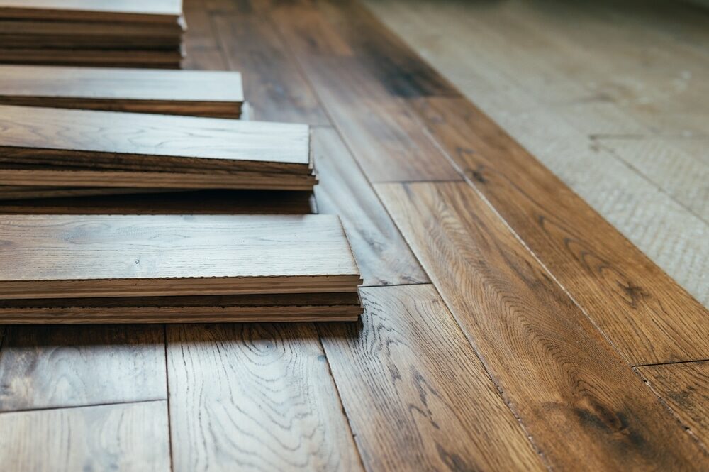 Stacked wooden floor planks beside an installed hardwood floor.