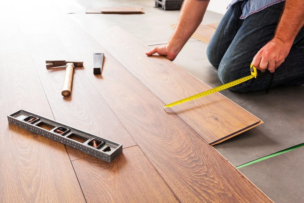 Person measuring wooden floorboards with a tape measure during installation.