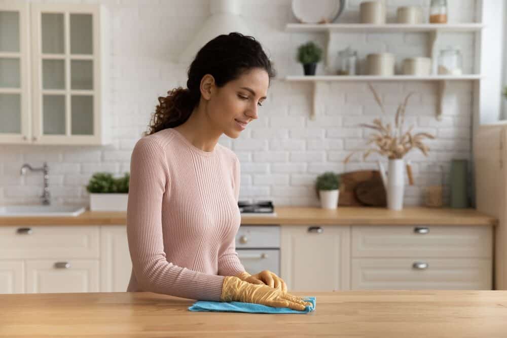 Woman in a pink sweater cleaning a kitchen countertop with a blue cloth.
