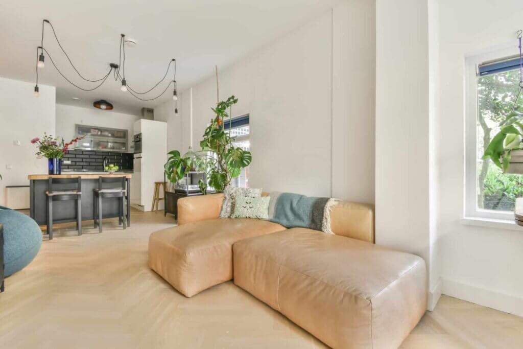 Living room in Hainault, UK, with a beautifully sanded and refinished herringbone parquet floor done by Mr Sander®. The room features a modern design with a tan leather sofa, indoor plants, and a kitchen island with bar stools.