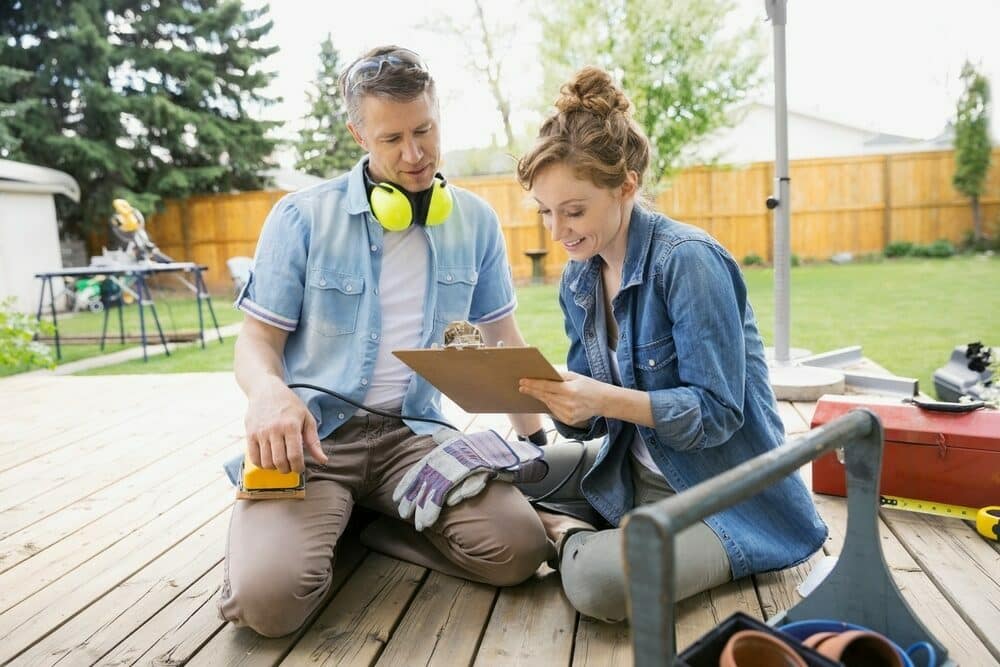 Two people reviewing a project plan on a wooden deck with tools around.