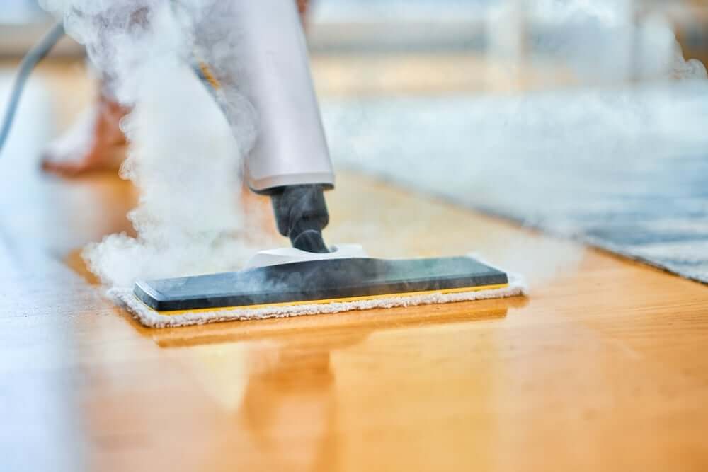 A steam mop cleaning a beautifully refinished wooden floor, emitting steam while in use. The floor appears shiny and well-maintained, showcasing the effectiveness of the cleaning process.