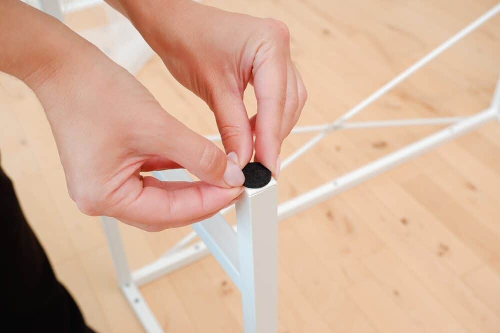 Close-up of hands fitting a protective felt pad onto the leg of a white chair.