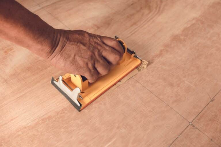 Hand using a manual laminate floor cutter on a wooden panel.