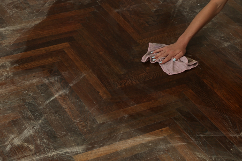 A person's hand wiping a herringbone patterned wooden floor with a cloth.