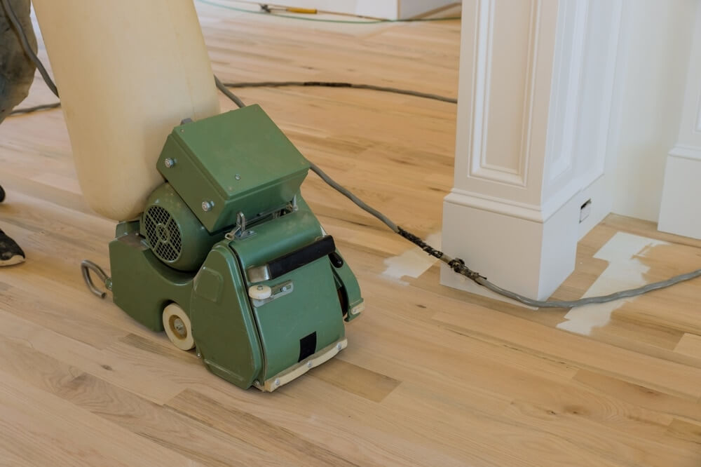 A man from Mr Sander® is sanding an oak floor in a living room in Rickmansworth, UK, using the Lagler HUMMEL. The HUMMEL features a powerful LED lighting system, high powered aggressive sanding, and extremely low dust emissions. It has a single-phase AC motor with 230 V / 50 CPS / 2.2 kW & thermal overload protection, a sanding drum width of 200 mm, drum speed of 2400 rpm, sanding belt dimensions of 200 x 750 mm, and a machine weight of 79 kg.
