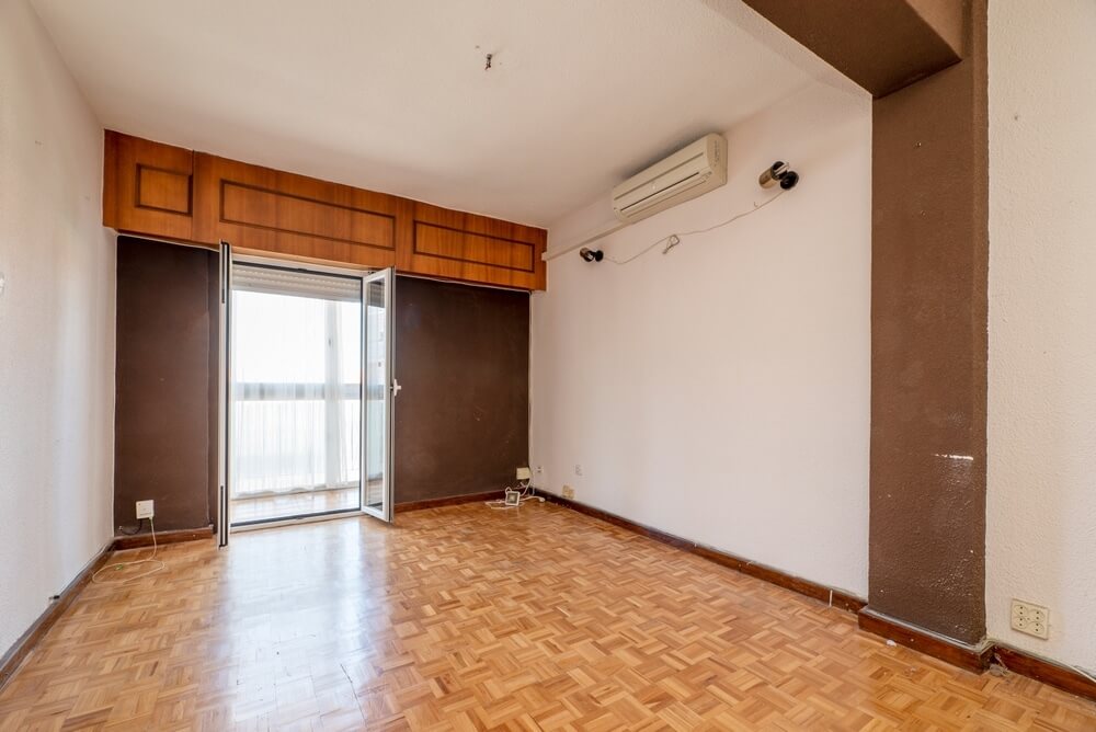 Interior view of a spacious room in Woodford Green, UK, featuring a parquet wood floor, an air conditioner mounted on the wall, and large windows leading to a balcony.