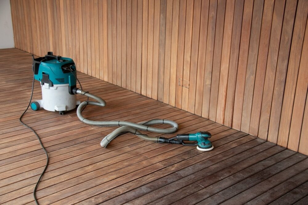 Electric sander and vacuum system on a wooden floor during a restoration process.