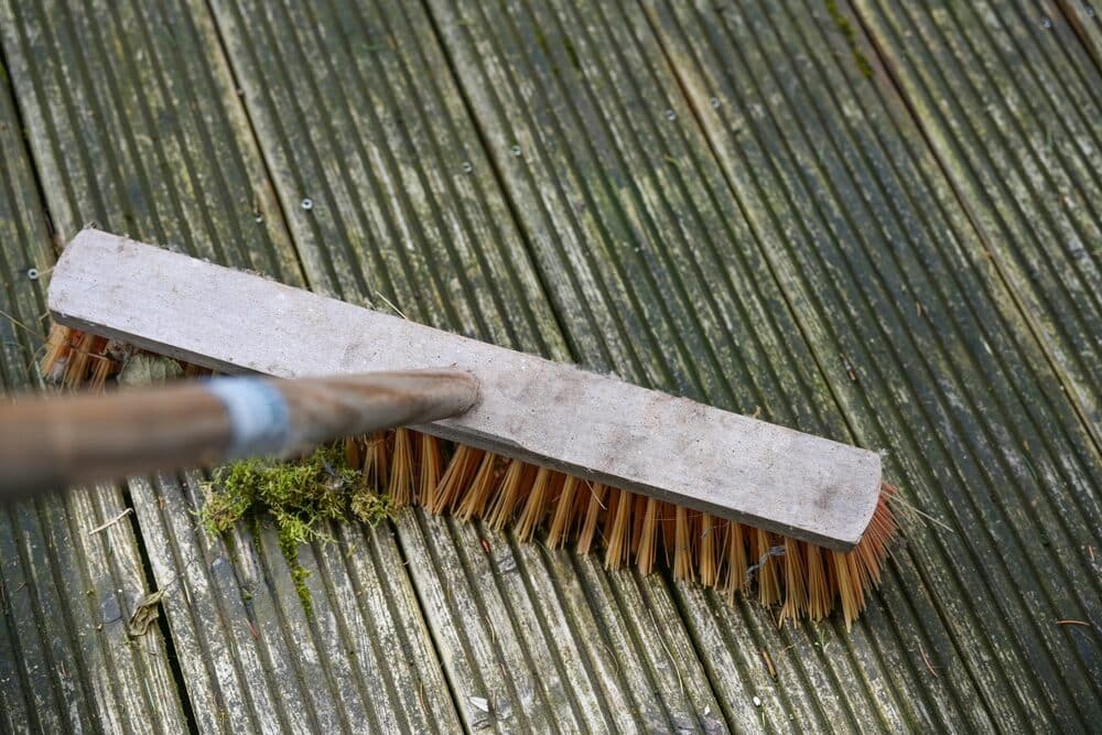 A stiff-bristle deck brush lying on a moss-covered wooden deck.
