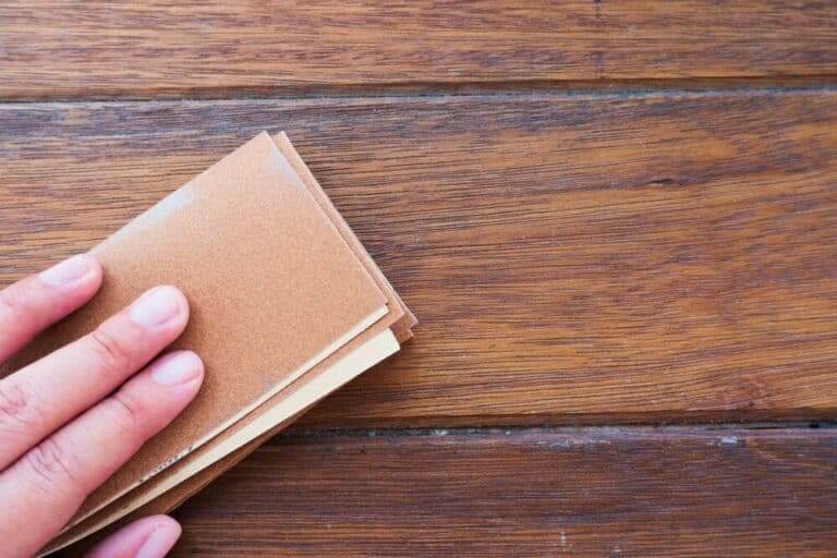 A hand holding a stack of sandpaper on a wooden surface.