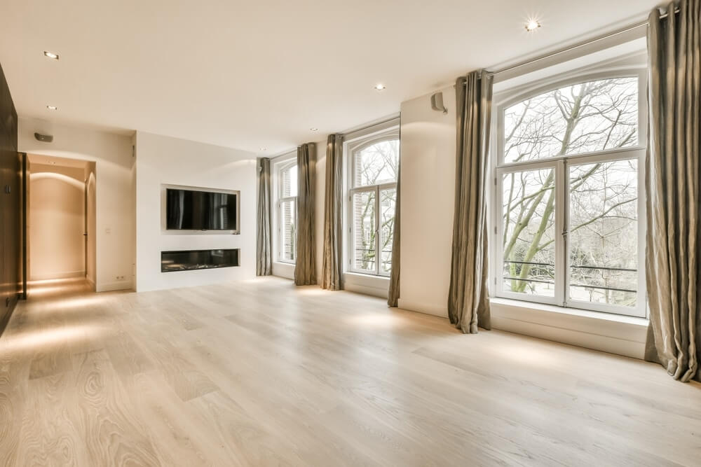 Luxurious living room in Hampshire, UK featuring large windows with elegant drapes, a modern built-in fireplace, and expertly refinished light oak flooring by Mr Sander®. The room is filled with natural light, highlighting the pristine finish and seamless craftsmanship of the wooden floor.