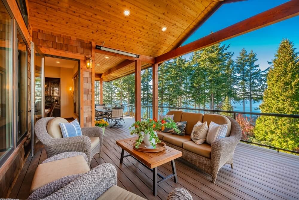 Beautifully finished wooden deck with comfortable outdoor furniture and scenic view of trees and water.