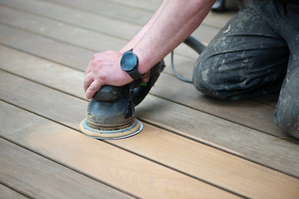 Close-up of a hand guiding an orbital sander on a wooden surface.