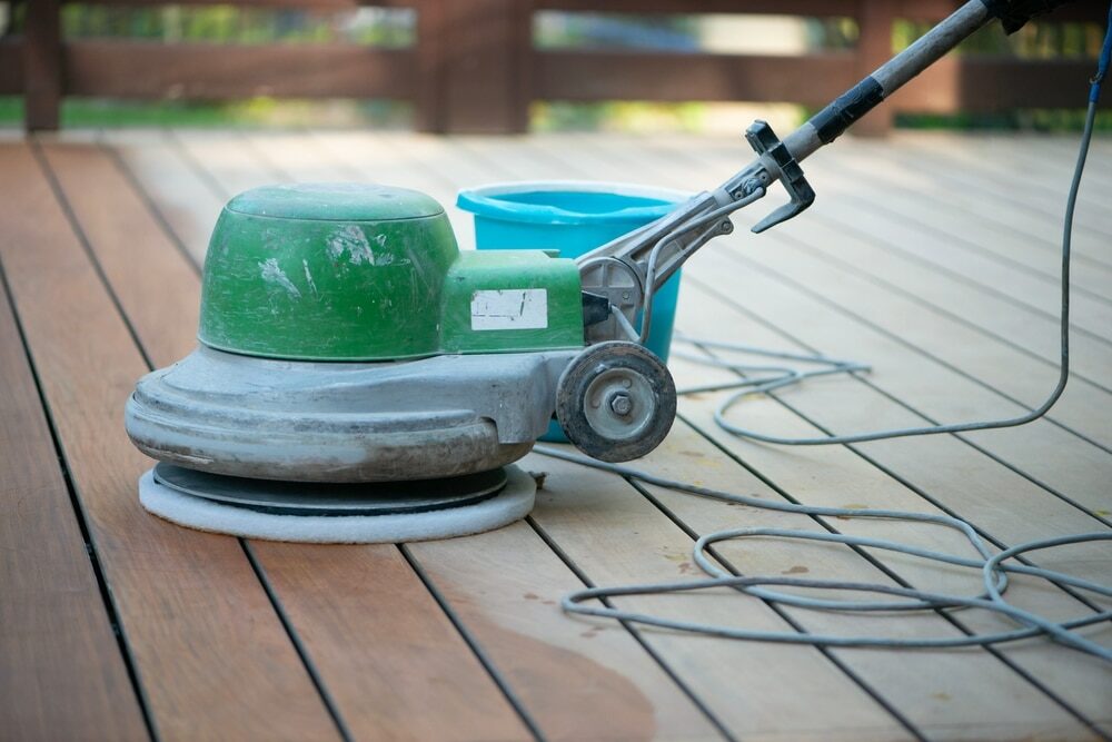 Floor buffer machine on a wooden deck with a bucket and mop in the background.