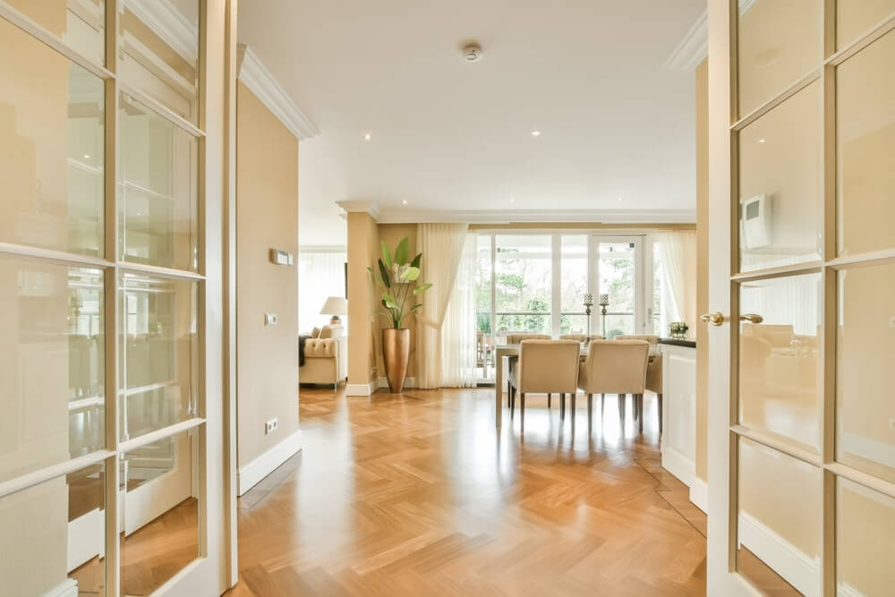 A spacious and elegantly furnished dining room with large windows and natural light highlighting the beautifully restored parquet flooring. The glossy, intricate pattern of the floor reflects the high-quality restoration work done by Mr Sander®.