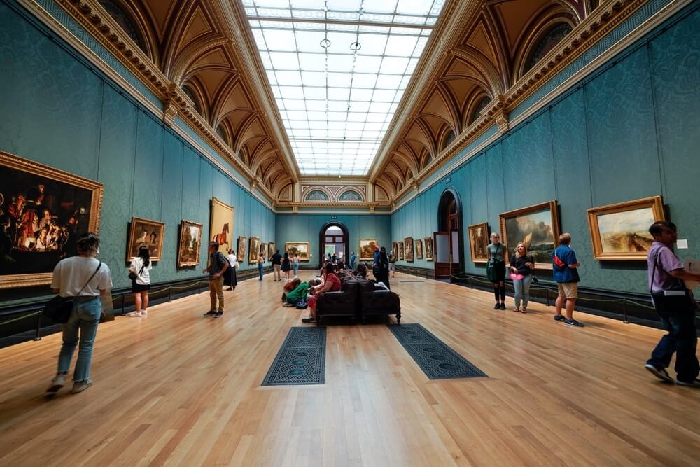 Visitors exploring an art gallery with beautifully refinished wooden floors and ornate architectural details.