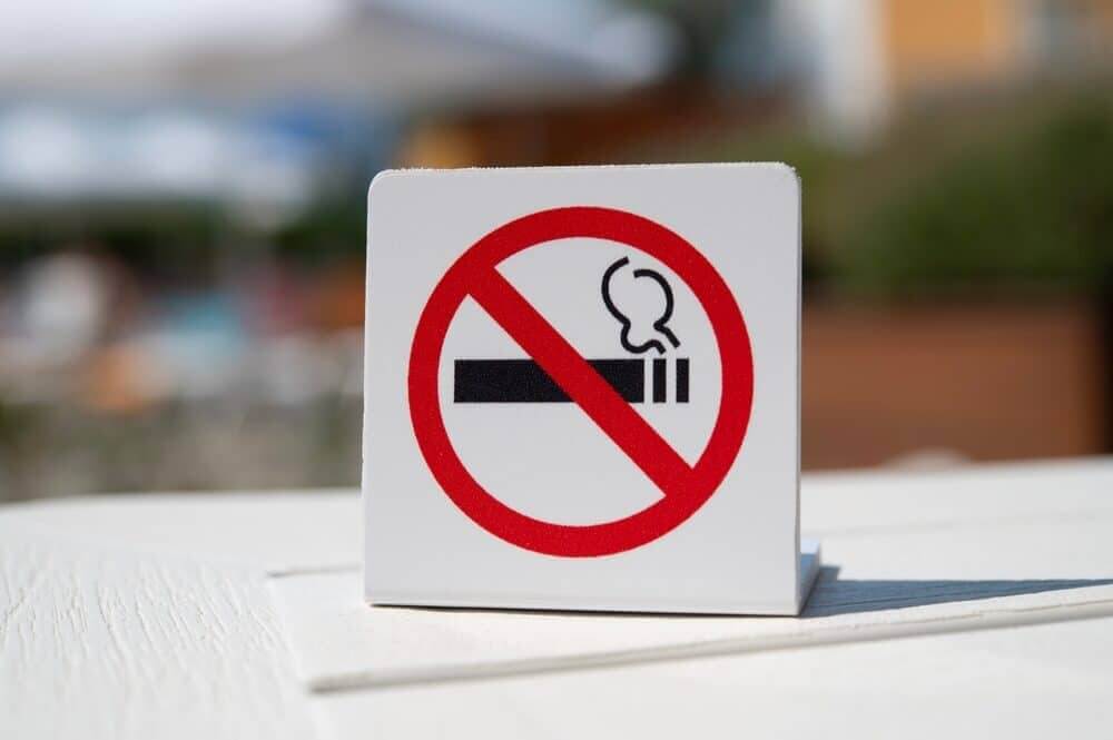 No smoking sign with a red prohibition circle over a cigarette icon, standing on an outdoor table.