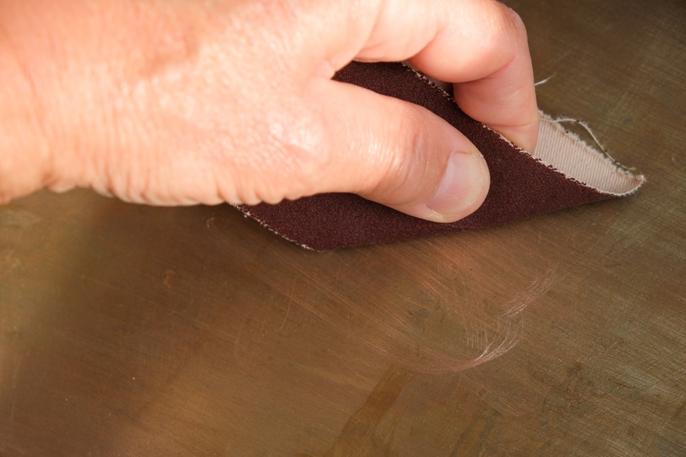 Close-up of a hand holding a piece of sandpaper, sanding a wooden surface.