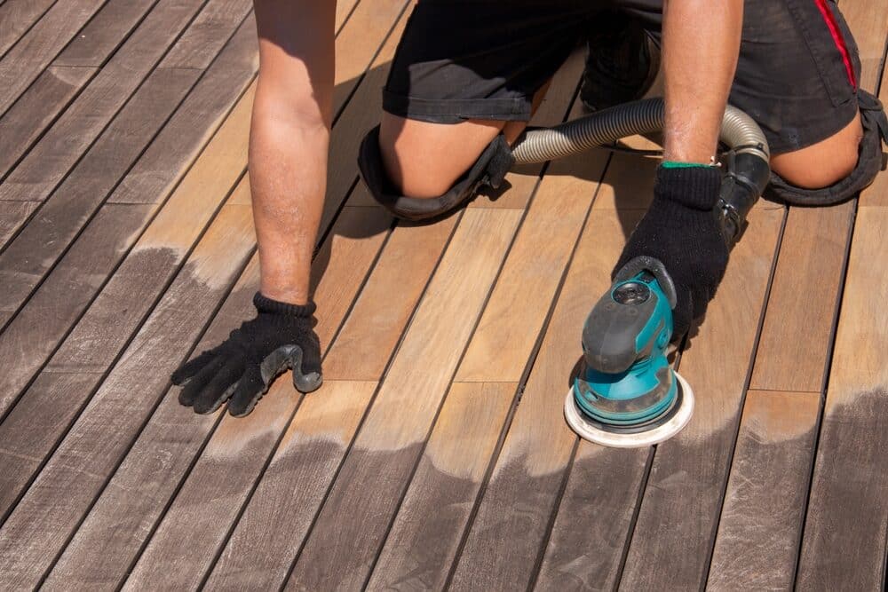 Close-up of a person sanding a wooden deck with an orbital sander.