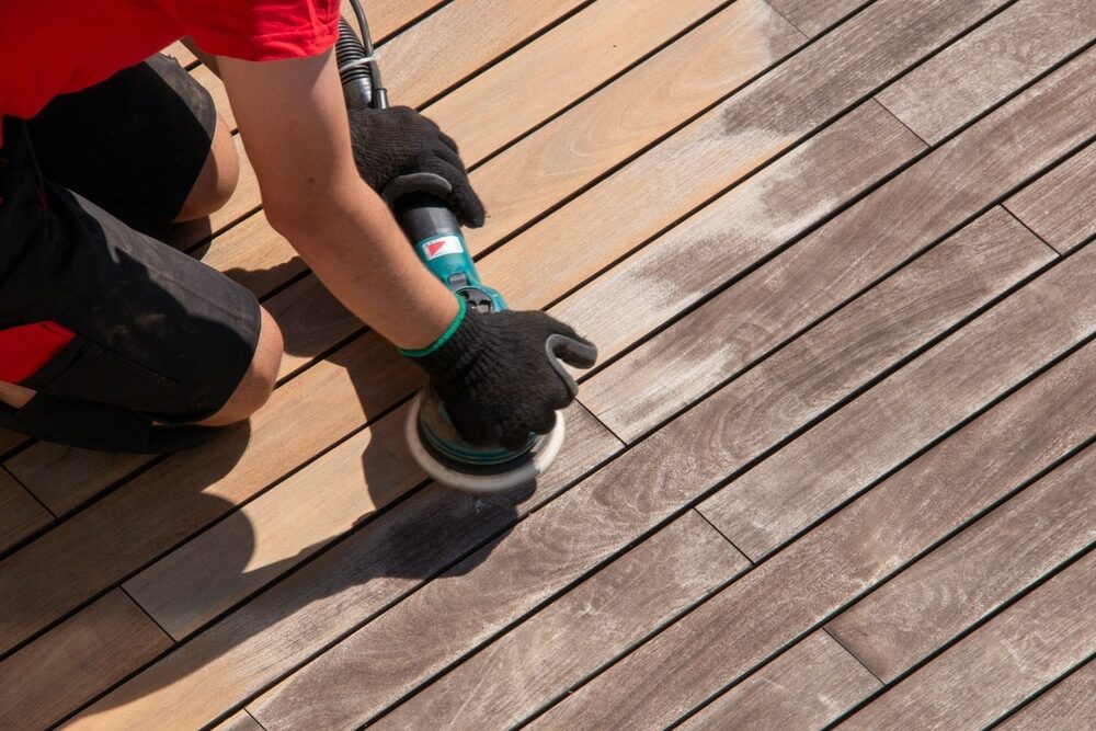 Person sanding a wooden deck with a handheld electric sander.