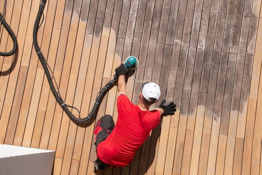 Worker sanding a wooden deck with an orbital sander.