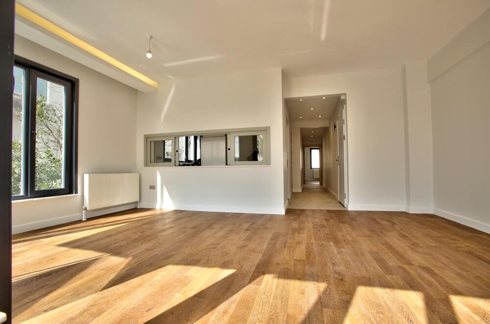 A bright and spacious room with newly sanded and refinished wooden flooring, large windows letting in ample natural light, and modern minimalist decor.