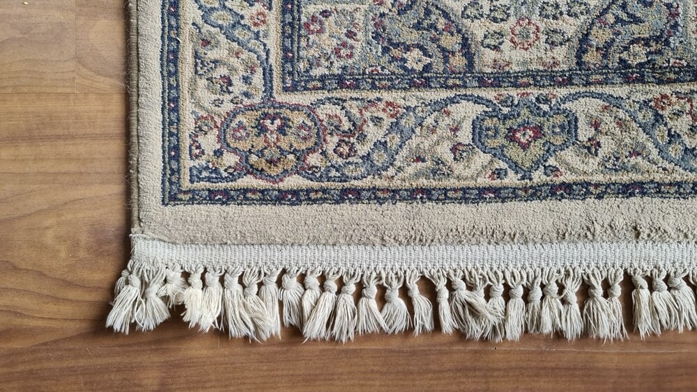 A close-up of a vintage patterned rug with tassels on a beautifully refinished hardwood floor.
