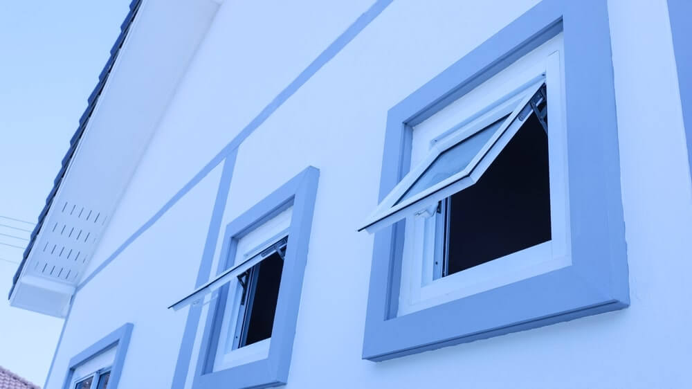 Two open windows on the side of a white house with blue trim, allowing ventilation, which is essential during processes like floor sanding to reduce dust accumulation indoors.