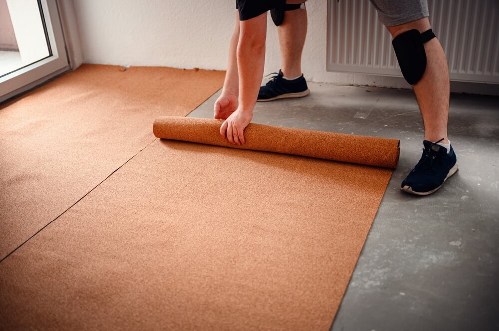A worker unrolling a sheet of cork flooring underlayment on a concrete floor.