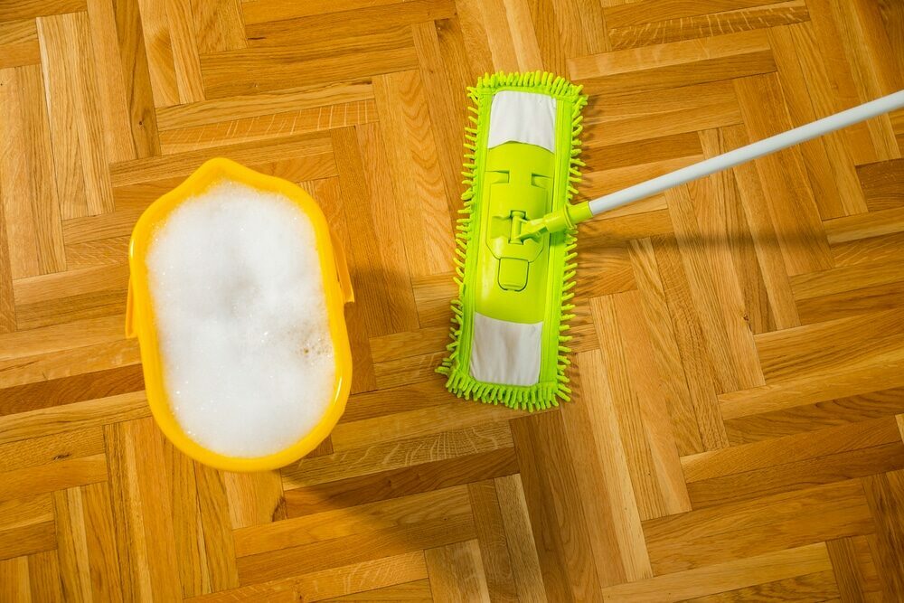 A yellow mop and bucket filled with soapy water on a parquet floor.