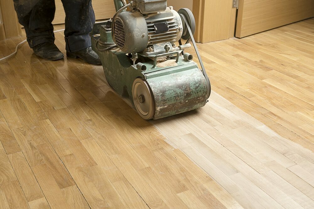 A floor sander machine being used on a hardwood floor in the process of refinishing.