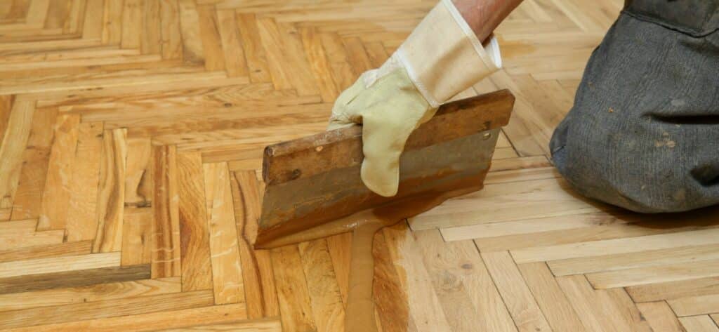 Top view of a person using a floor sanding machine on parquet flooring, with sawdust collection bag attached.