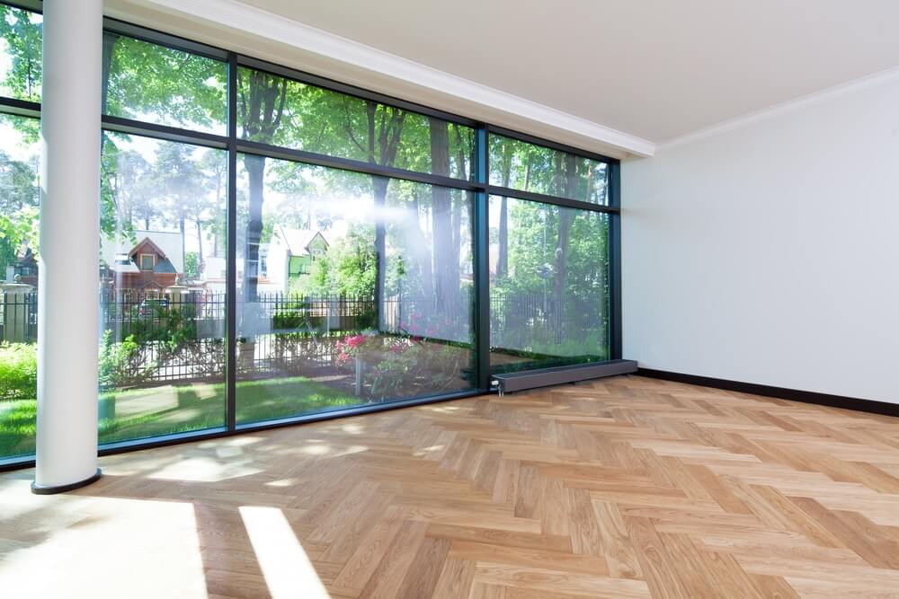Spacious room with large floor-to-ceiling windows overlooking a lush garden in Westcombe Park, UK. The room features beautifully refinished herringbone parquet flooring, showcasing the expert floor sanding and refinishing work by Mr Sander®.