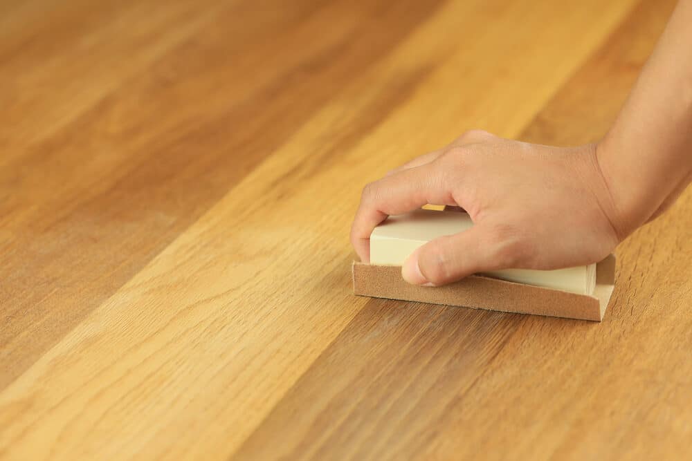 Hand sanding a wooden surface with a sanding block.