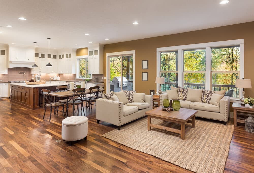 Open concept living space with a seating area, dining set, and kitchen, featuring large windows with a view of autumn foliage.
