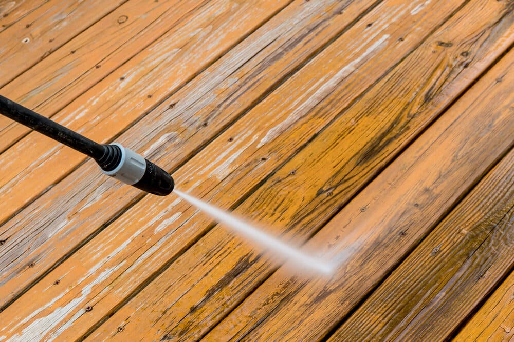 Pressure washing a weathered wooden deck, cleaning and restoring the wood's appearance.