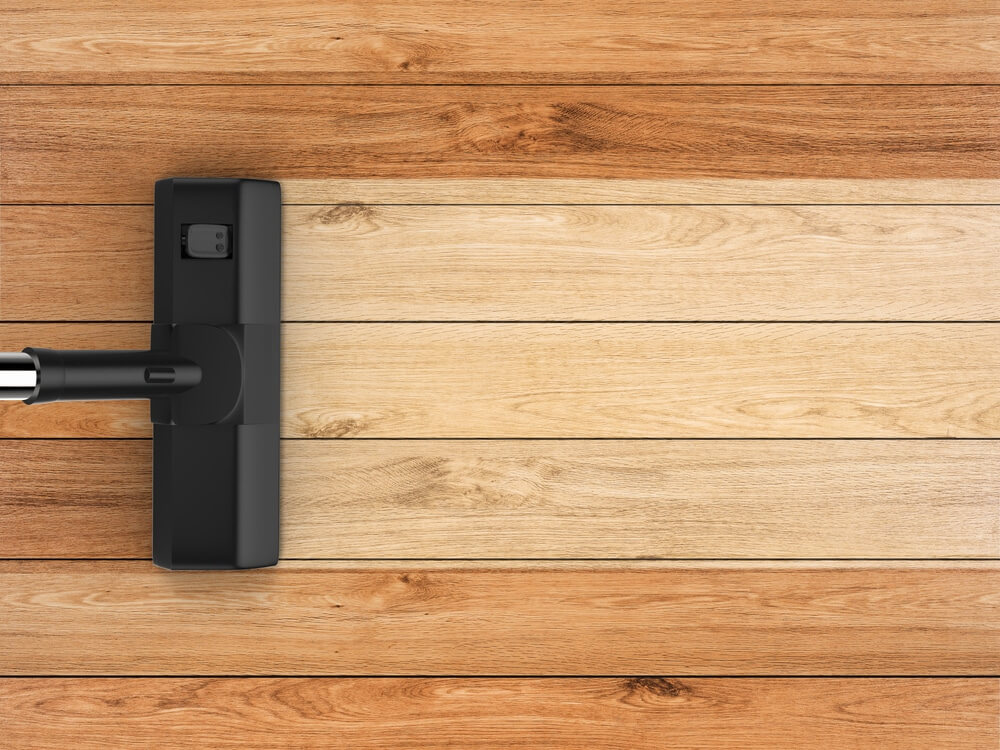 An overhead view of a hardwood floor featuring three distinct wood tones—light, medium, and dark—highlighting the natural beauty of the wood grain. A vacuum cleaner attachment is positioned over the floor, suggesting maintenance and care after the sanding and refinishing process completed by Mr. Sander®. The various shades reflect the richness of the wood, likely oak or walnut, emphasizing the quality of the refinishing work.