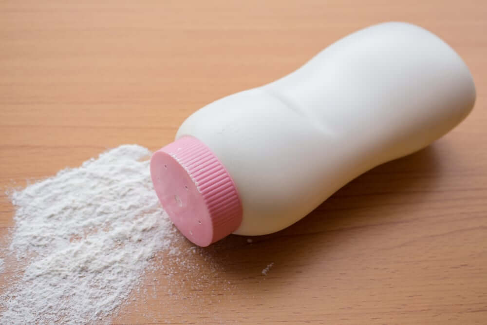 A white talcum powder container with a pink cap lying on its side, spilling powder onto a polished wooden surface.