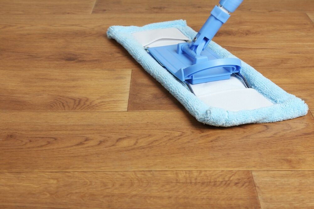 A blue mop with a microfiber pad gliding over a shiny hardwood floor.