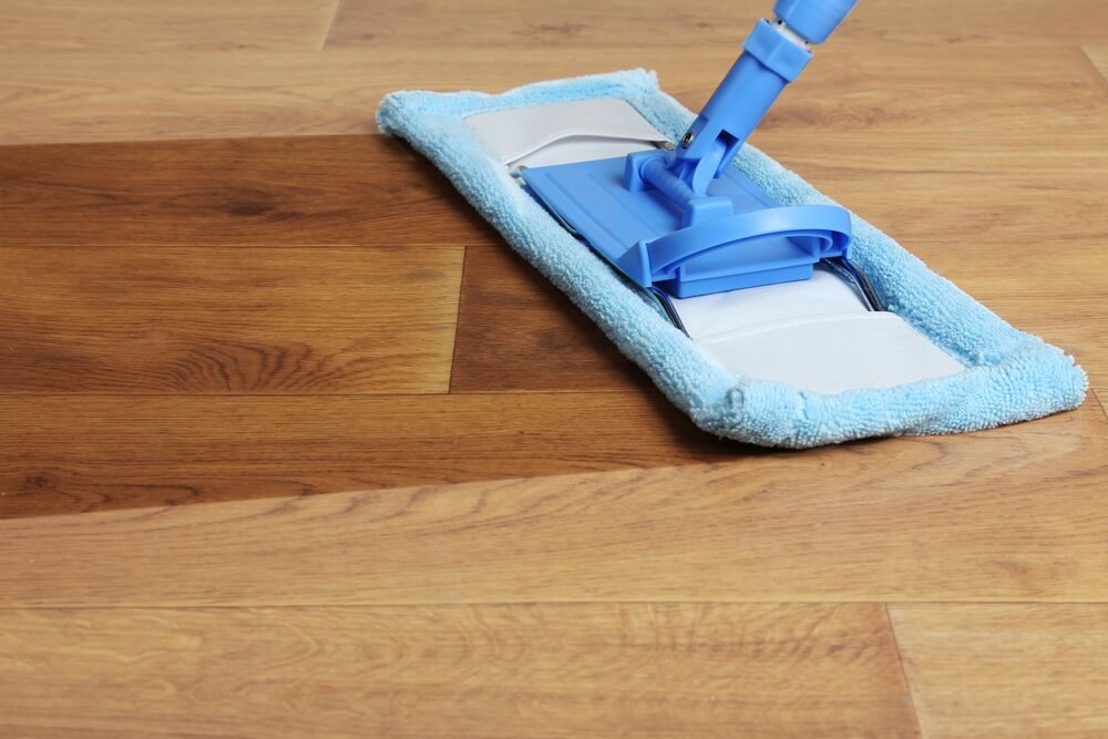 A close-up view of a blue microfiber mop cleaning a beautifully refinished wooden floor. The image highlights the smooth, polished surface of the wood, showcasing the high-quality floor sanding and refinishing services provided by Mr Sander®.    