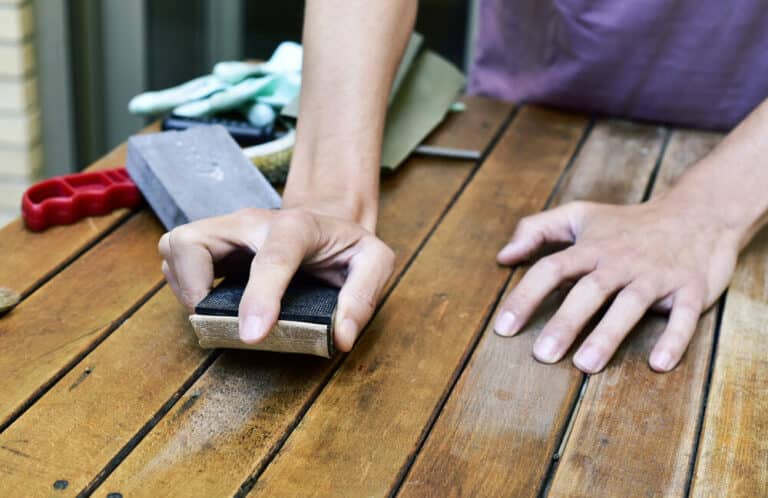 Person sanding a wooden table with a hand-held sanding block.