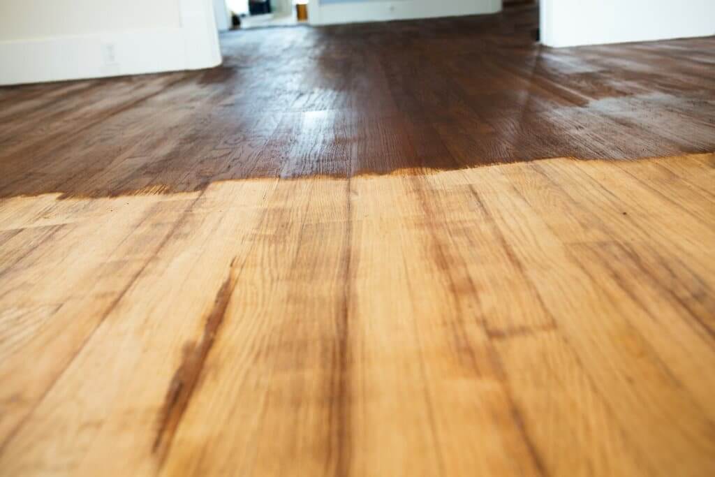 Can I Stain My Wood Floors Without Sanding? - A hardwood floor partially sanded and stained, showing a clear distinction between the light, unfinished wood and the dark, finished wood.