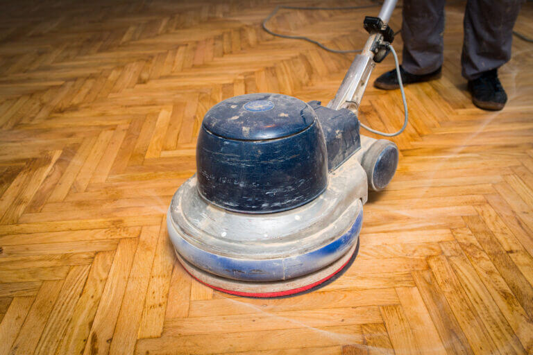 A person using a professional floor buffer to polish a wooden floor